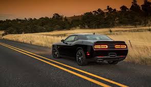 A black Dodge Challenger driving past a field. A Diminished Value Appraiser in Raleigh, North Carolina call 772-359-4300.